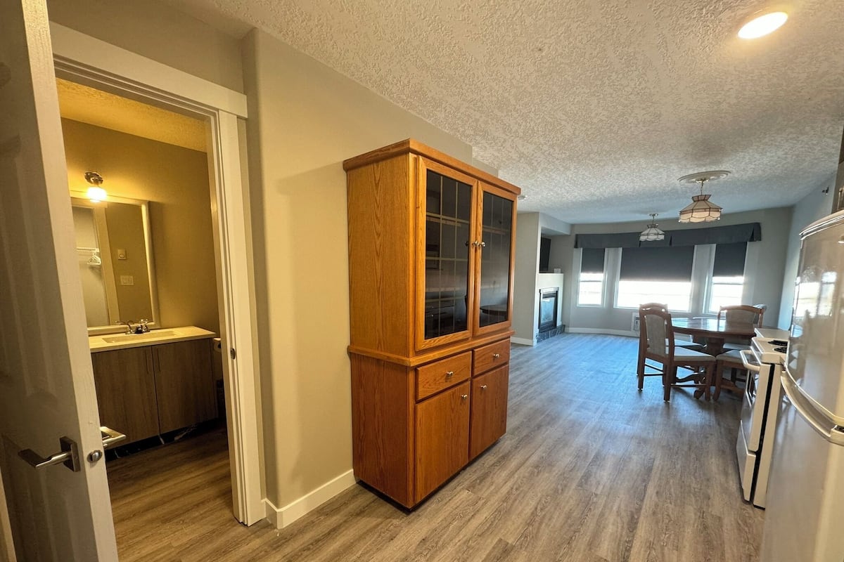 A spacious living area with a wooden cabinet, a dining table with chairs, and a kitchen area with a refrigerator.