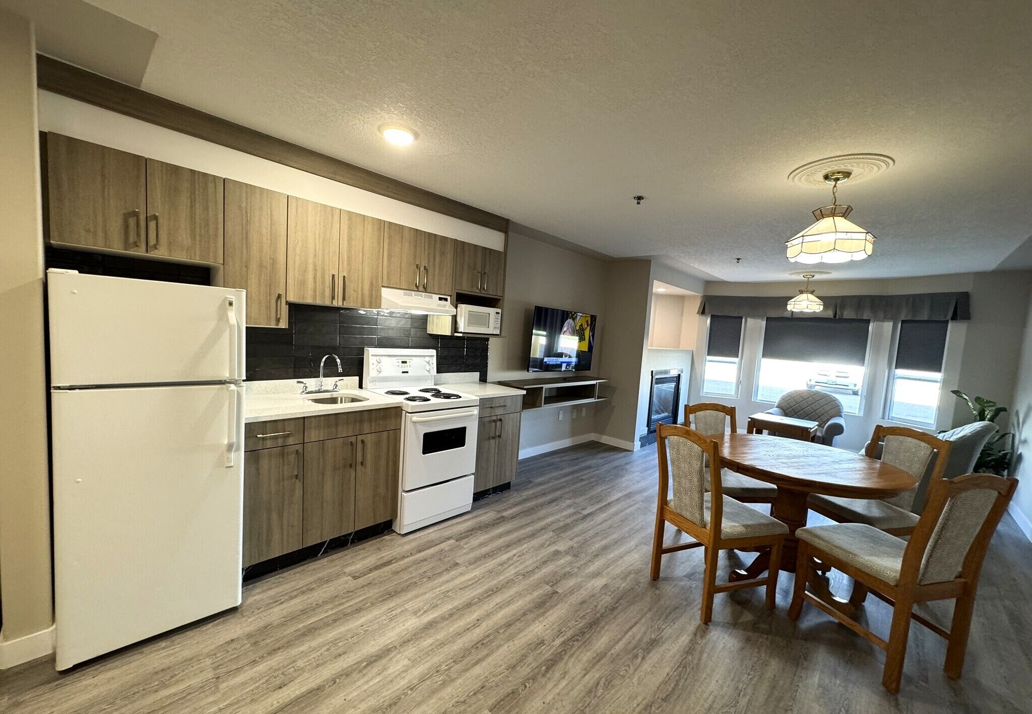 A modern kitchen with wooden cabinets, a white refrigerator, a stove, and a dining area with a wooden table and chairs.