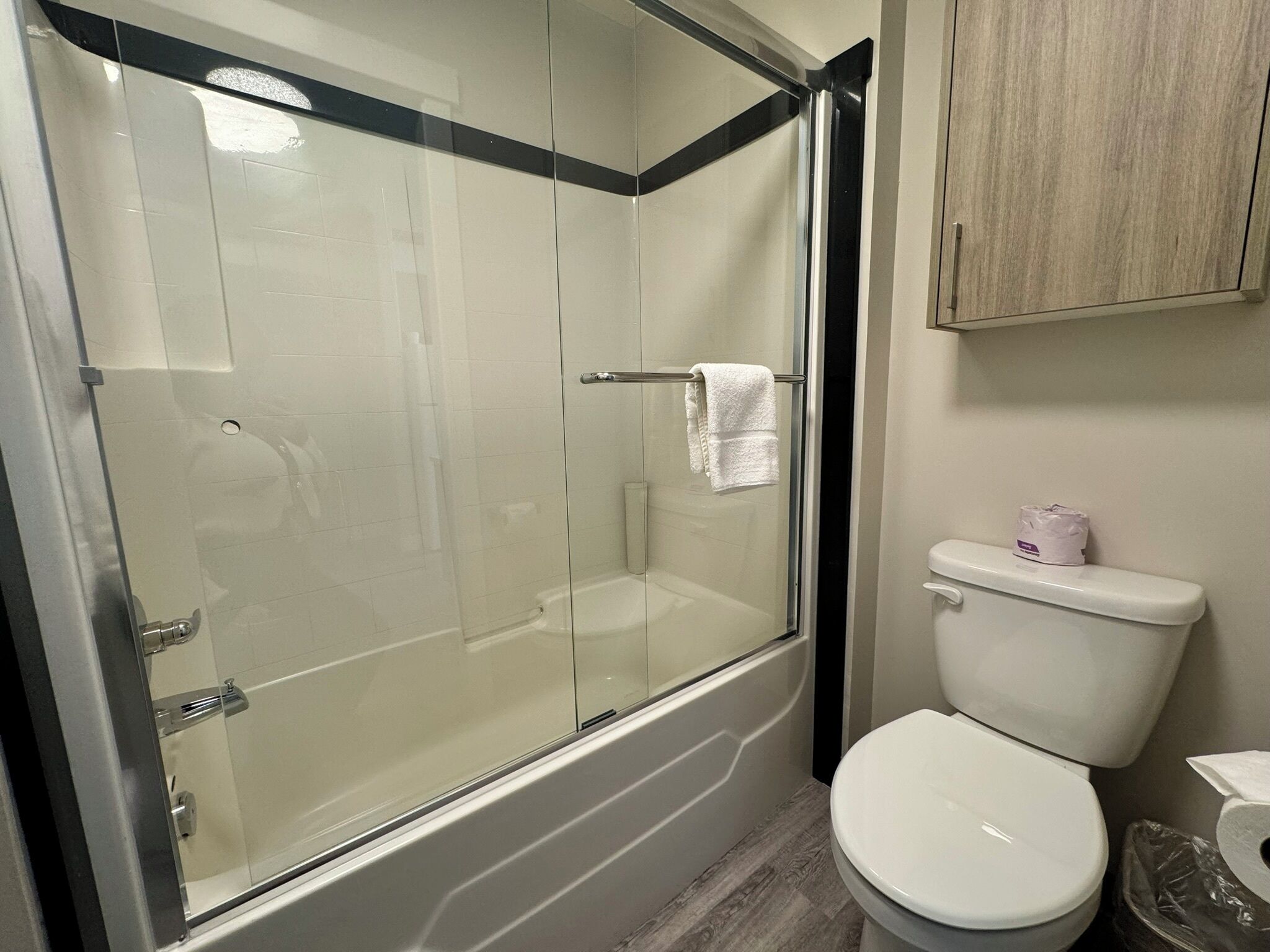 Un baño con ducha de vidrio, inodoro blanco y mueble de madera.