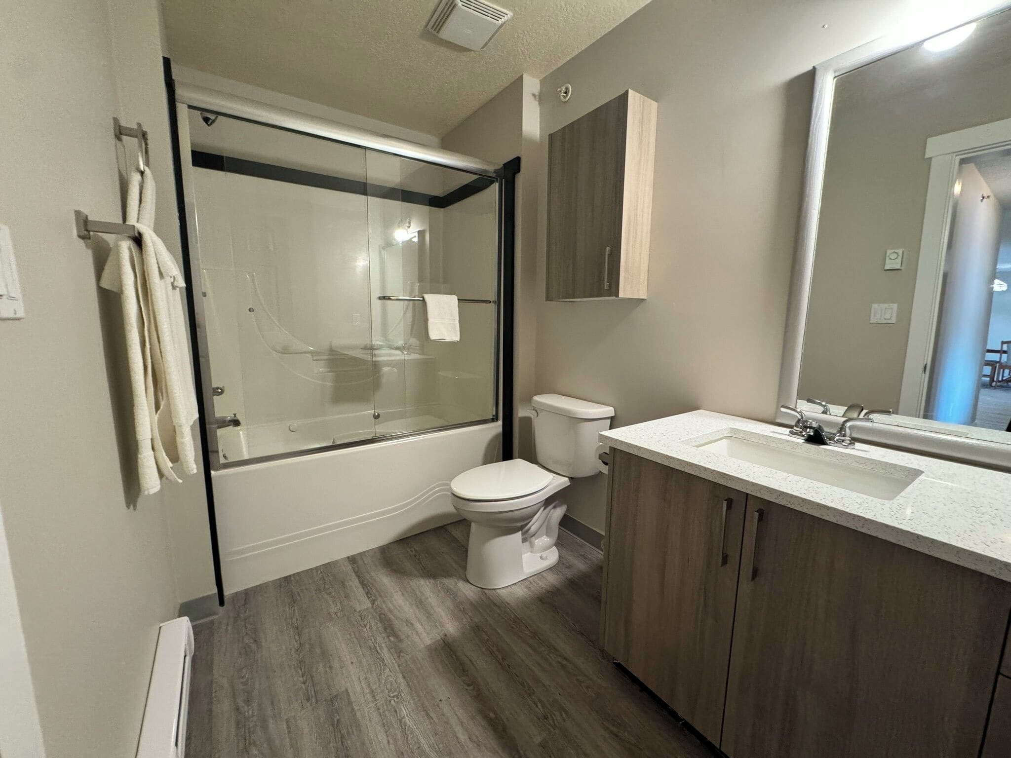Une salle de bain moderne avec une douche à parois de verre, des toilettes blanches et un meuble-lavabo en bois doté d’un grand miroir.