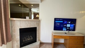 A living room with a fireplace, a television mounted on a wall, and a wooden desk with drawers. - Western Budget Motel - Ponoka (Ponoka)