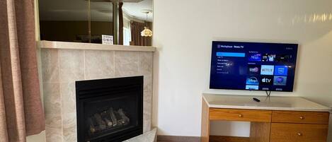 A living room with a fireplace, a television mounted on a wall, and a wooden desk with drawers.