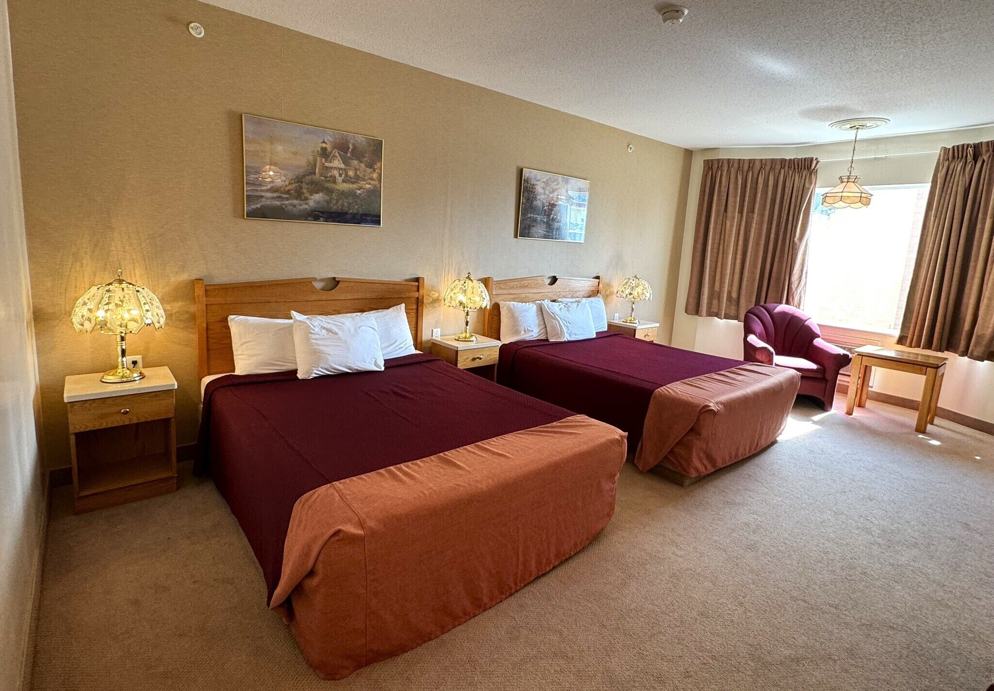 A hotel room with two beds, a desk, a chair, and two lamps.