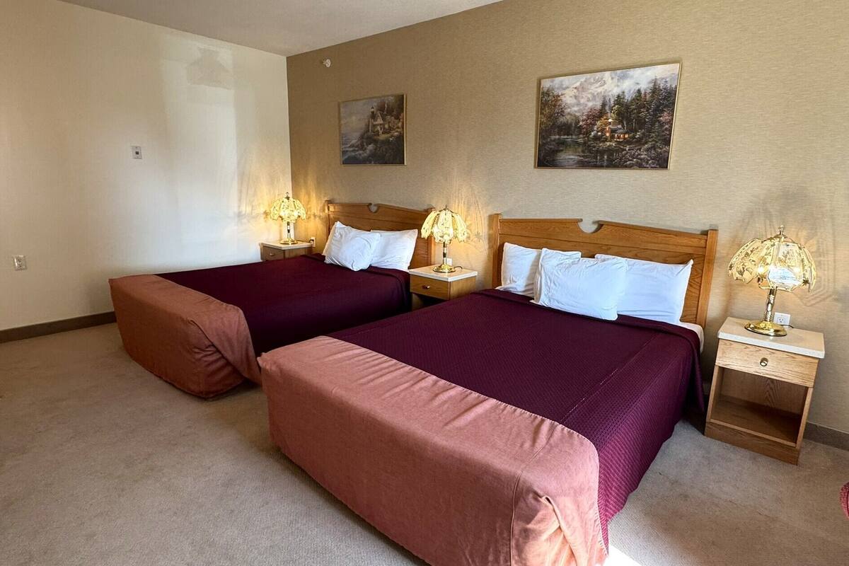 A hotel room with two beds, each with a wooden headboard, and two nightstands with lamps.