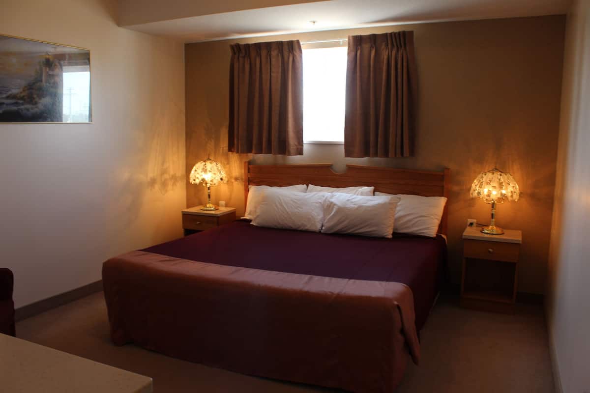 A hotel room with a large bed, two bedside lamps, a nightstand, and a window with curtains.
