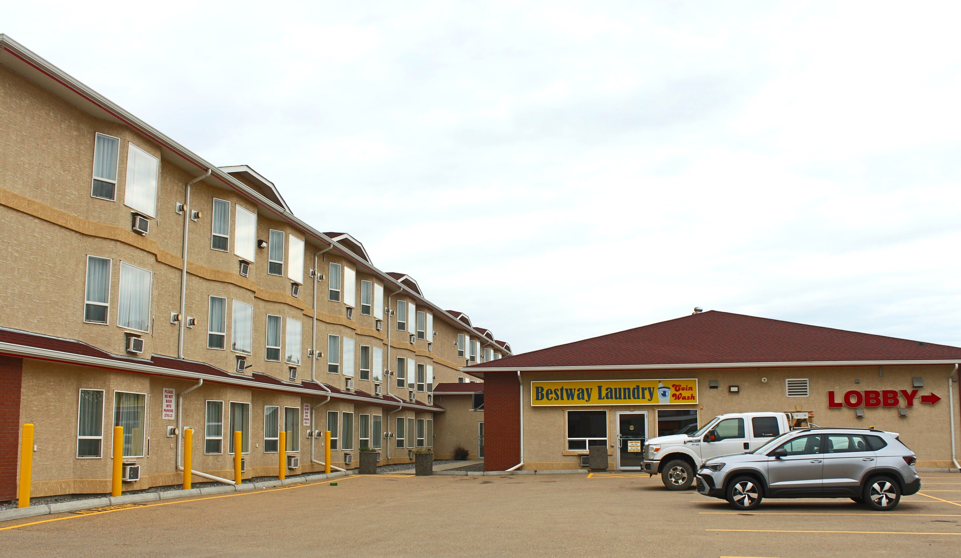 A multi-story motel with a 'Lobby' sign, a 'Bestway Laundry' service, and a parking area with a white SUV.