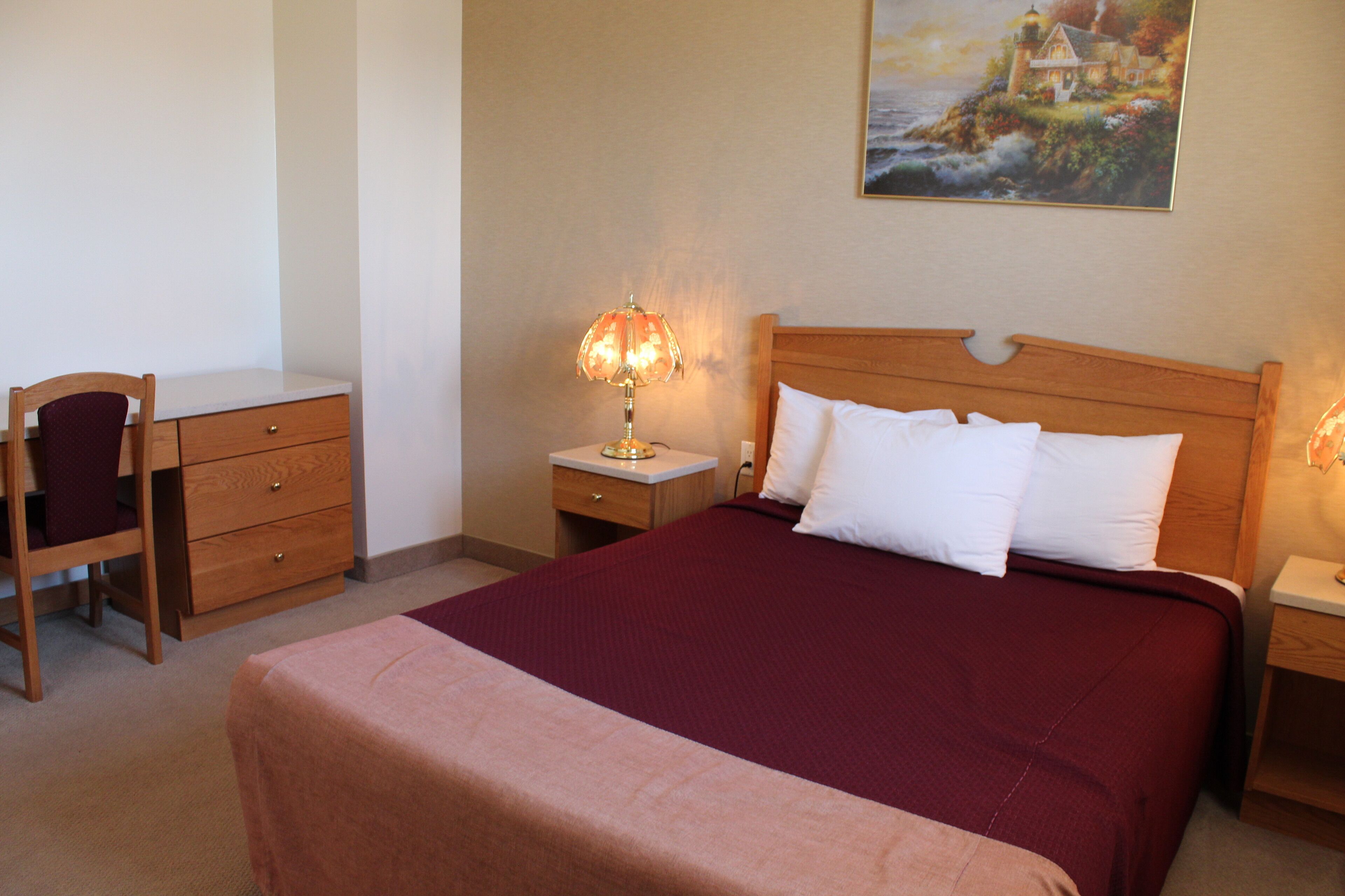 Une chambre d’hôtel bien rangée, avec un lit, un bureau, une chaise et une table de chevet avec une lampe.