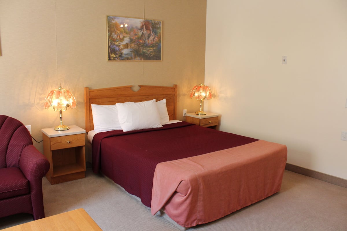 A bedroom with a wooden bed, two bedside tables with lamps, a chair, and a painting on the wall.