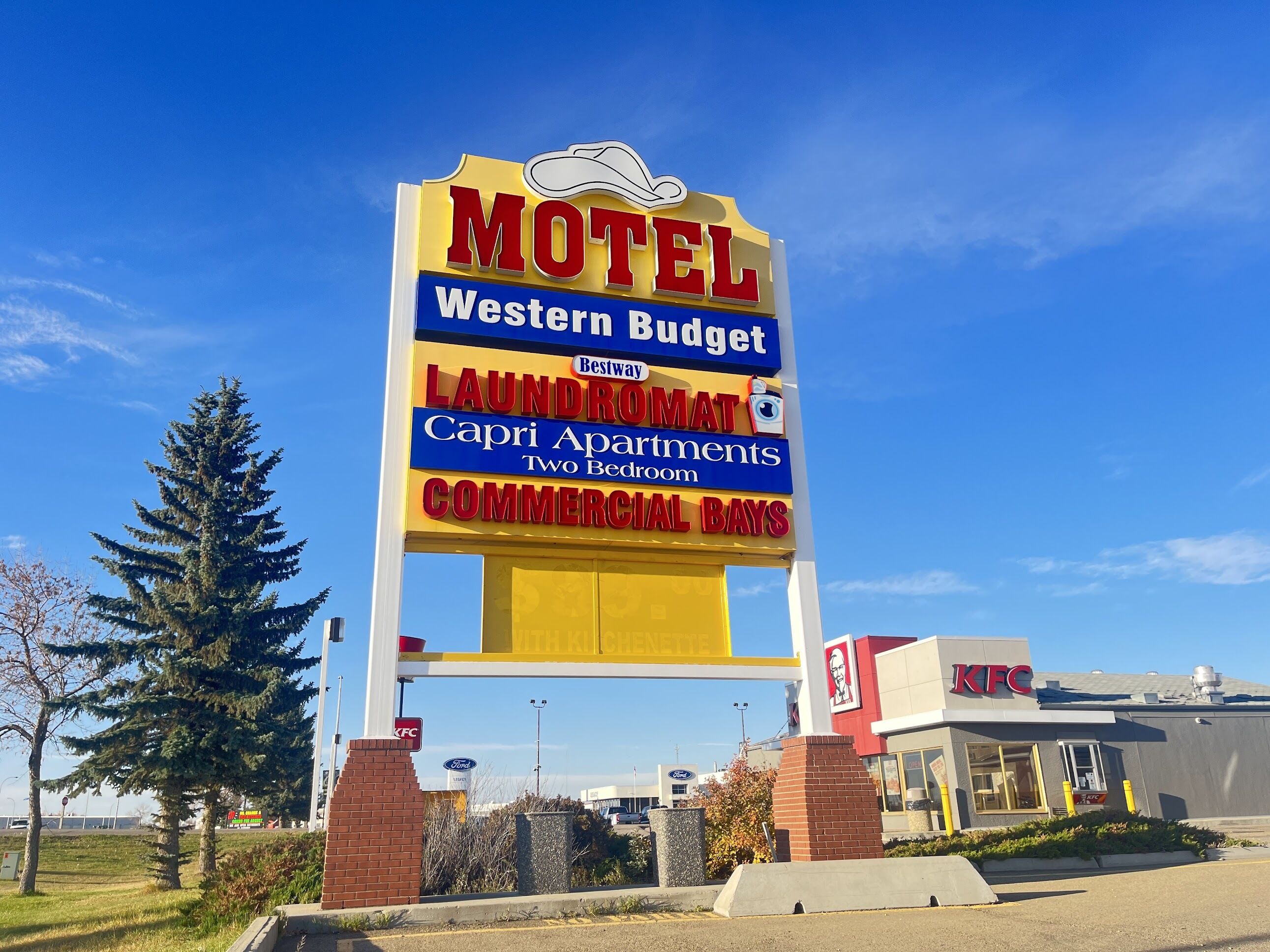 Letrero de motel con logotipo Western Budget, servicios de lavandería, Capri Apartments con dos habitaciones y locales comerciales.