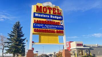 Letrero de motel con logotipo Western Budget, servicios de lavandería, Capri Apartments con dos habitaciones y locales comerciales.