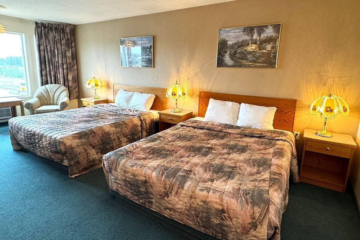A hotel room with two beds, a chair, and a window.