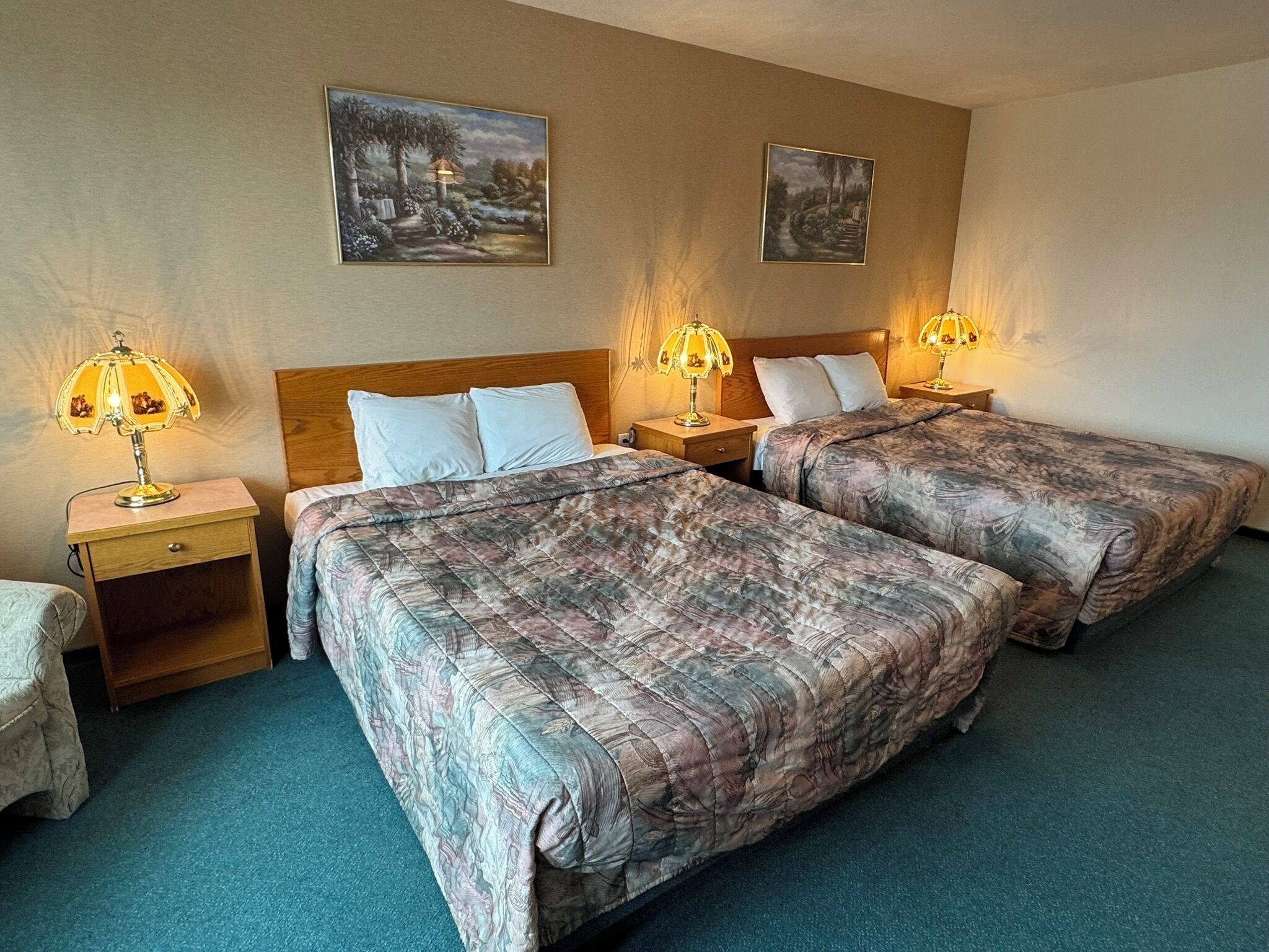 A hotel room with two beds, wooden headboards, and bedside lamps.