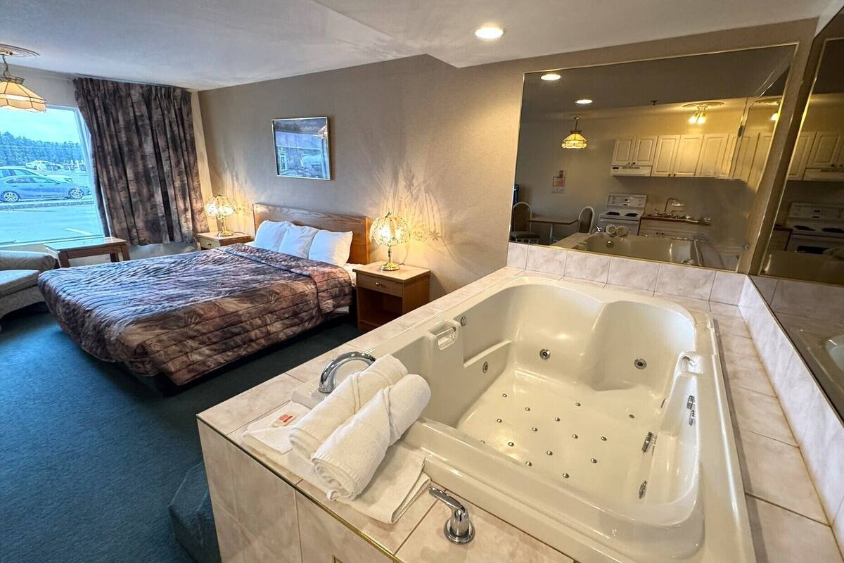 A hotel room with a large bed, a separate bathroom with a jacuzzi, a window with curtains, and a view of the parking lot.