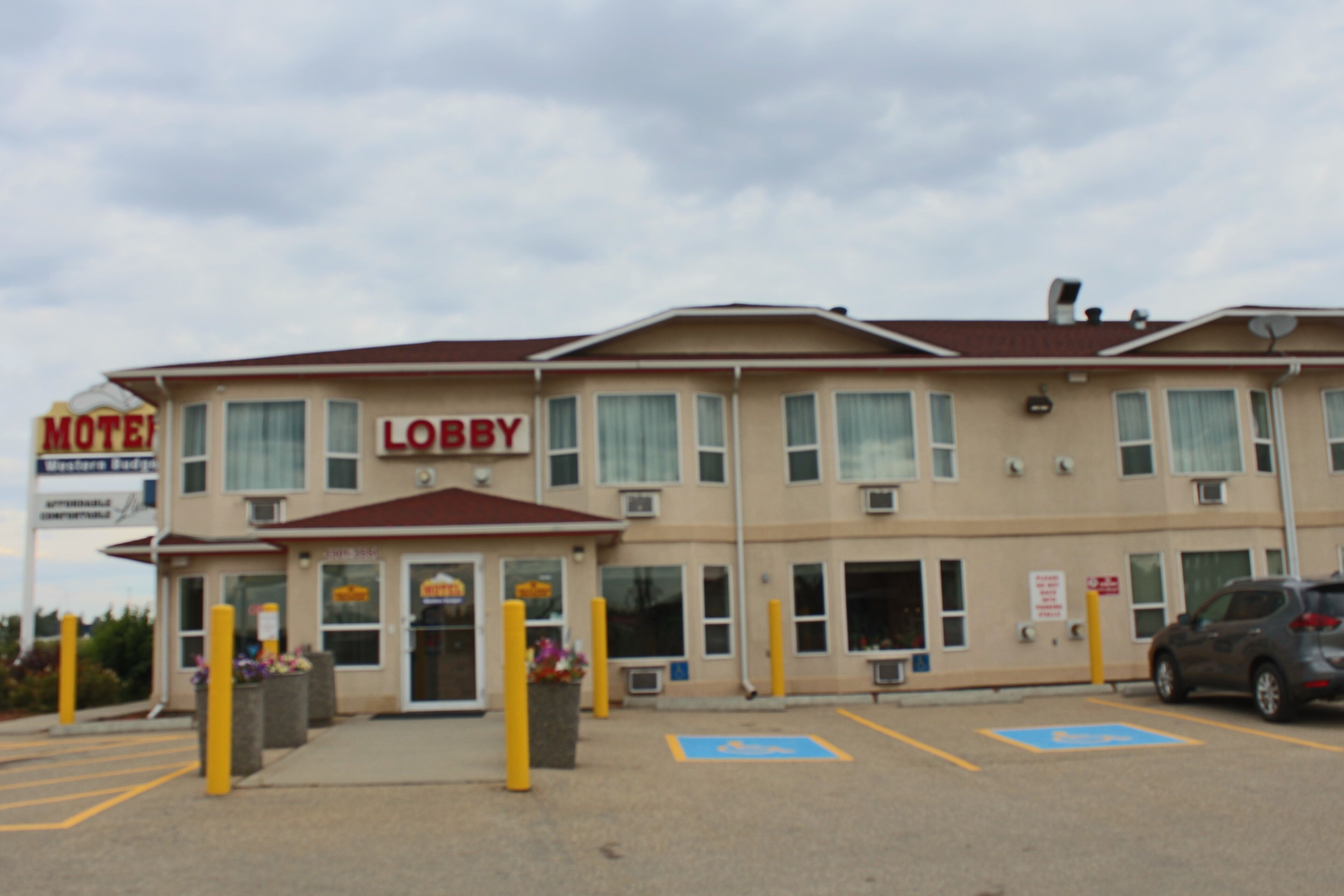 A motel with a sign reading "Motel Lobby." It features a parking lot with marked spaces and a building with multiple windows and air conditioning units.
