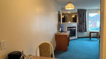 A compact hotel room with a kitchenette, a dining area with a table and chairs, a small TV, and a view of the street.
