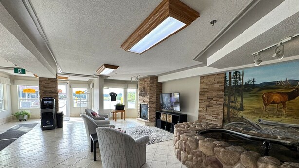 A spacious lobby with a stone fireplace, comfortable seating, and a mounted television. - Western Budget Motel Whitecourt 3 (Whitecourt)