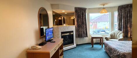 Een hotelkamer met een bureau, een televisie, een open haard, een bed en een raam met gordijnen.