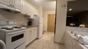 A modern kitchen with white cabinets, a stove, and a refrigerator. There is a wooden countertop and a sink. - Western Budget Motel Whitecourt 3 (Whitecourt)