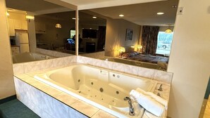 A modern bathroom with a large bathtub, a mirror, and a view of the bedroom through the mirror. - Western Budget Motel Whitecourt 3 (Whitecourt)