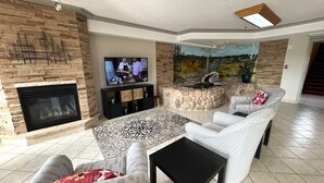 A living room with a stone fireplace, a flat-screen TV, a stone accent wall, and a patterned rug. - Western Budget Motel Whitecourt 3 (Whitecourt)