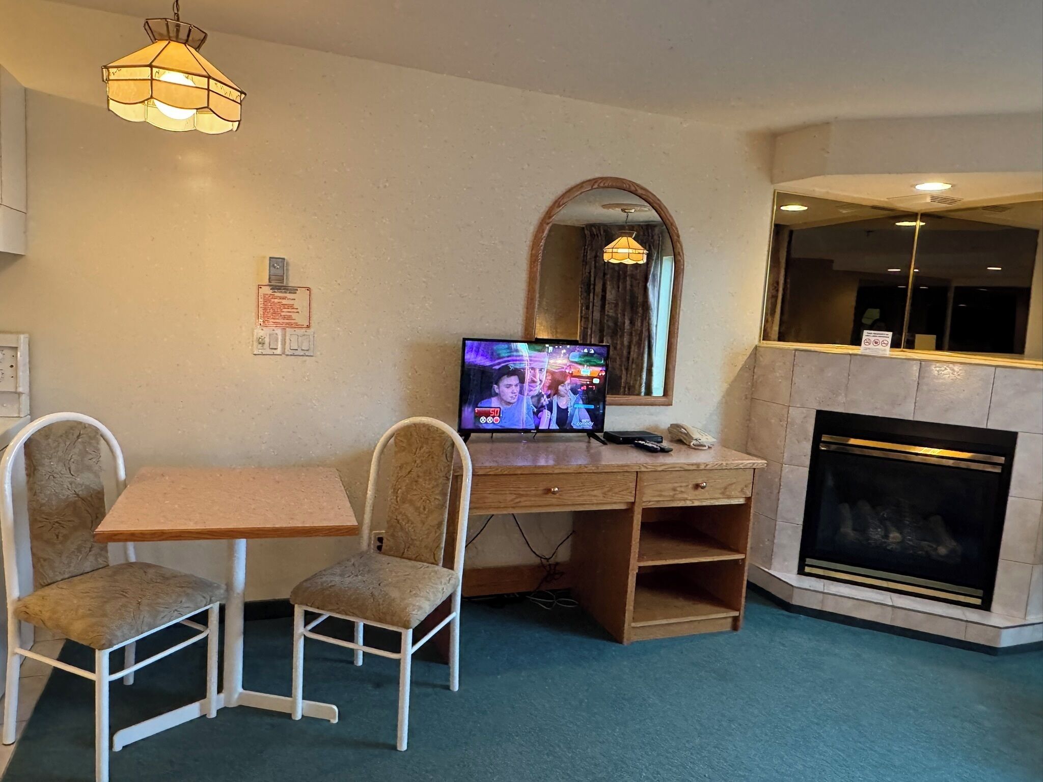 Une chambre d’hôtel avec un bureau en bois, deux chaises, une télévision, une cheminée et un miroir.
