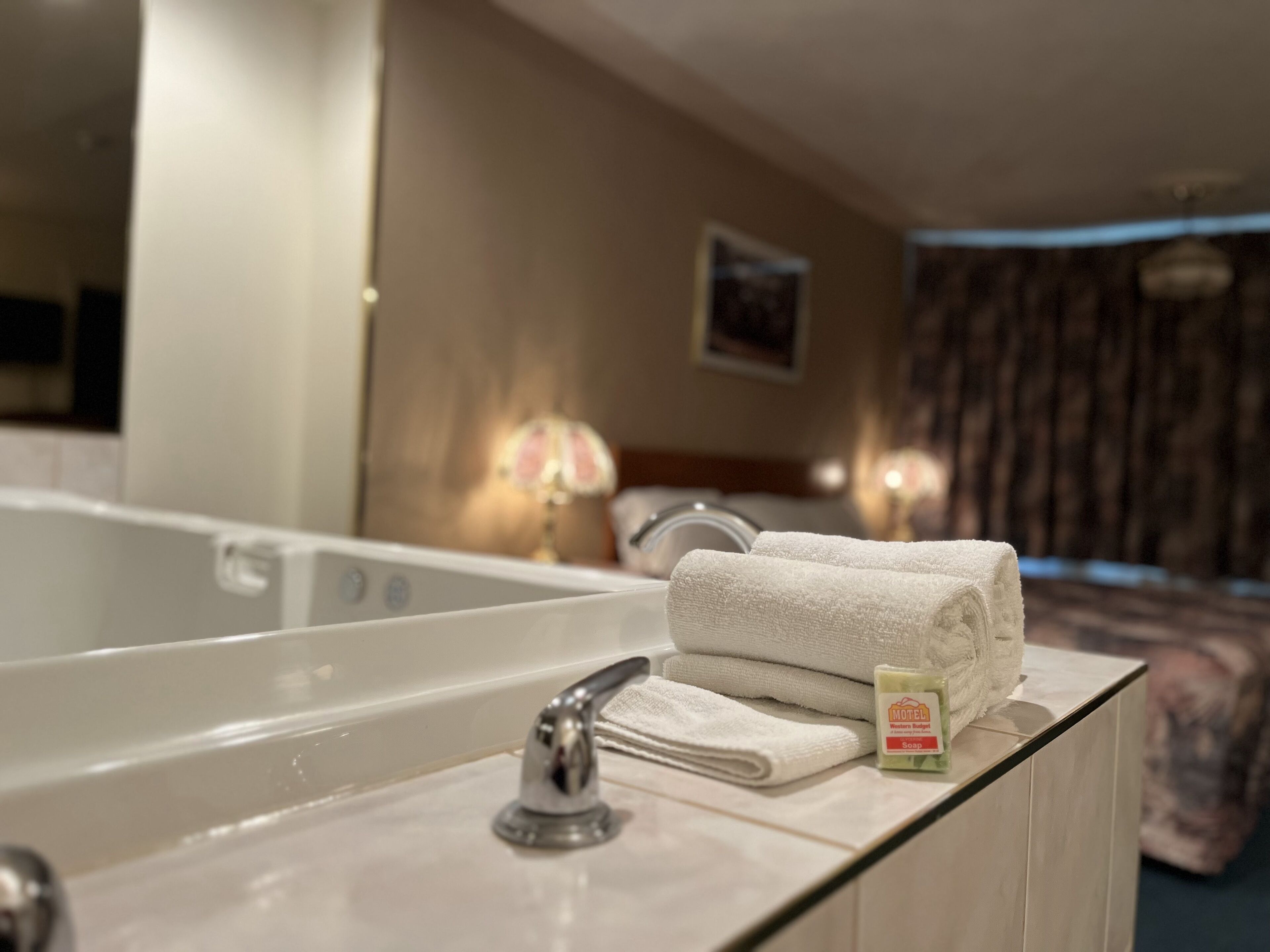 A bathroom with a bathtub, a sink, and a mirror. There are towels and a soap dispenser on the counter.
