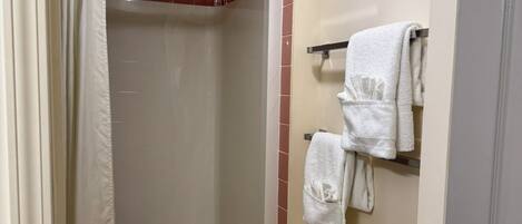 A bathroom with a shower, a towel rack with towels, and a radiator.