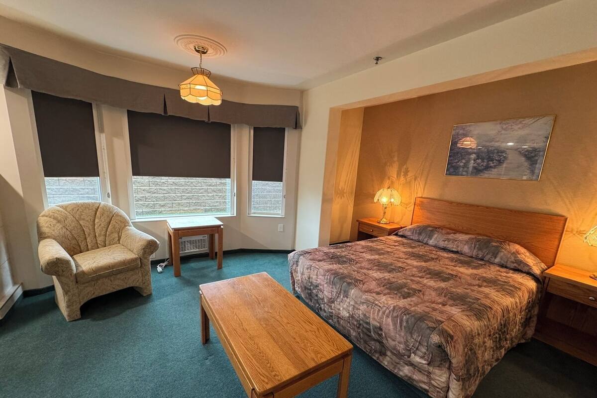 Une chambre d’hôtel avec un lit, une chaise, une petite table et un tableau au mur.