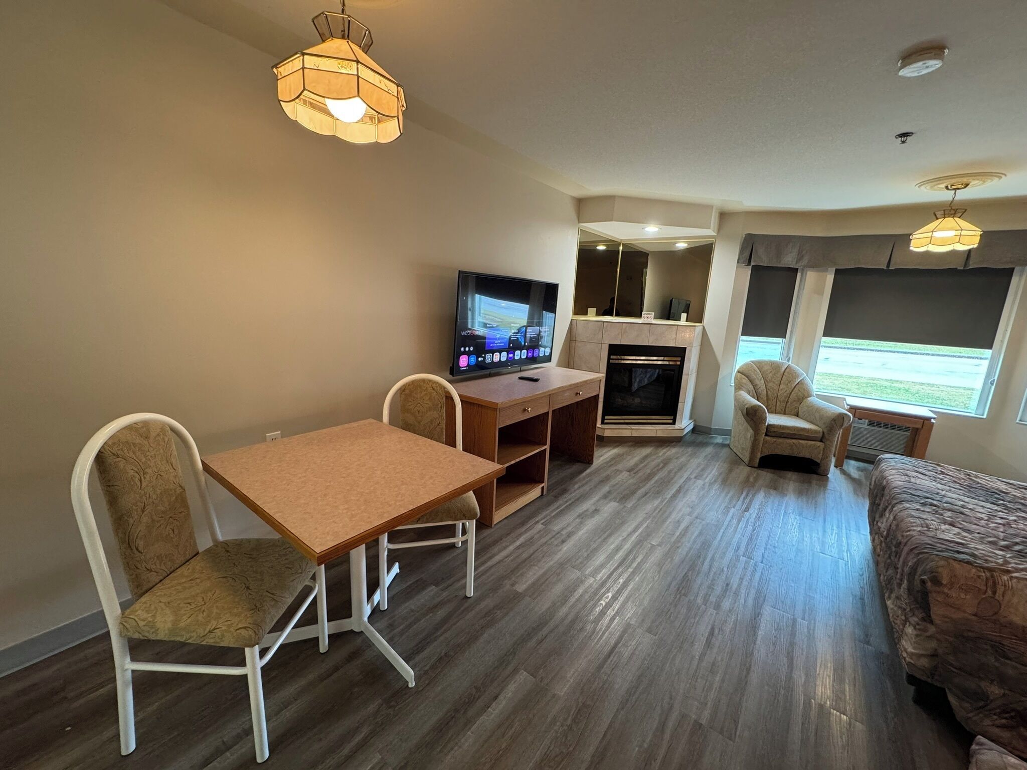 Ein möbliertes Zimmer mit Holztisch, zwei Stühlen, einem Fernseher, einem Kamin und einem Fenster mit Blick.