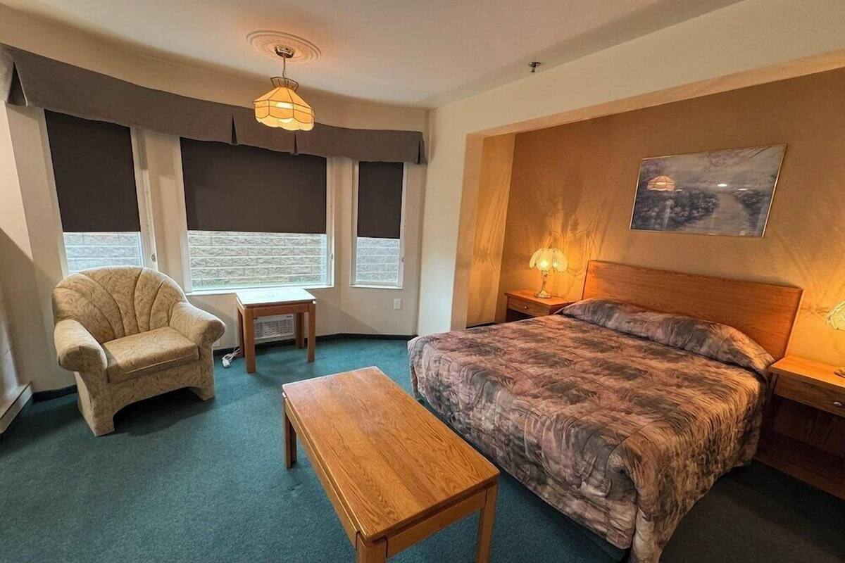 Une chambre à coucher avec un lit, une chaise, une table, une lampe et un tableau accroché au mur.
