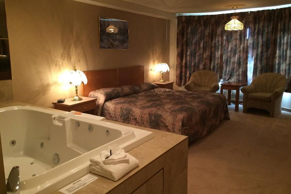 Une chambre d’hôtel avec une grande baignoire, un lit avec une tête de lit, deux lampes de chevet, une chaise et une petite table.