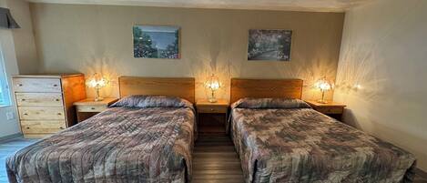 Quarto duplo com duas camas, cada uma com cabeceira e mesas de cabeceira com abajures. Há duas pinturas penduradas na parede acima das camas.