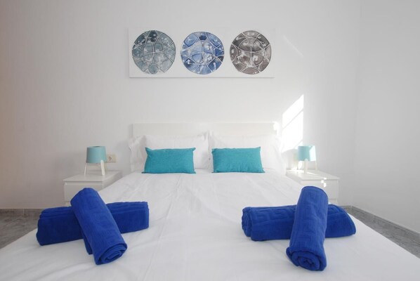 A hotel room with a large bed, two blue towels, two teal pillows, and three wall art pieces.