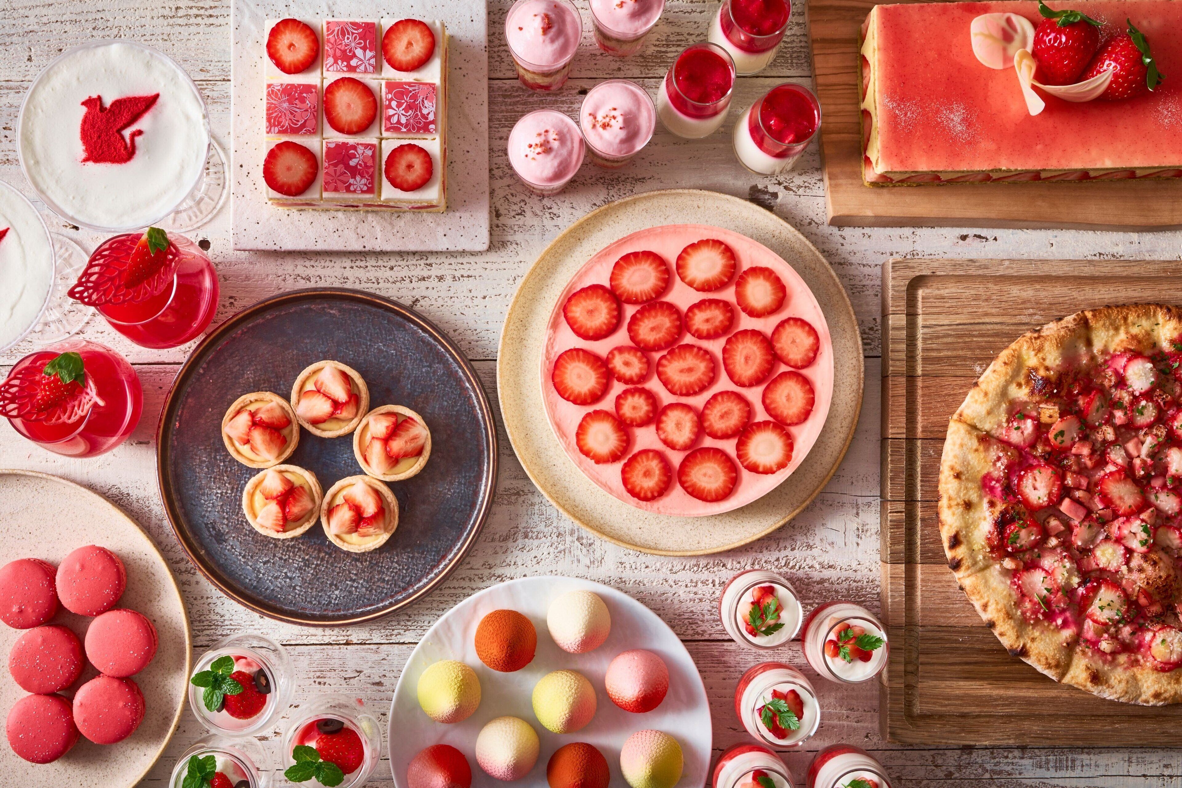 A variety of desserts including a strawberry tart, mini tarts, macarons, and a pizza topped with strawberries and cheese.