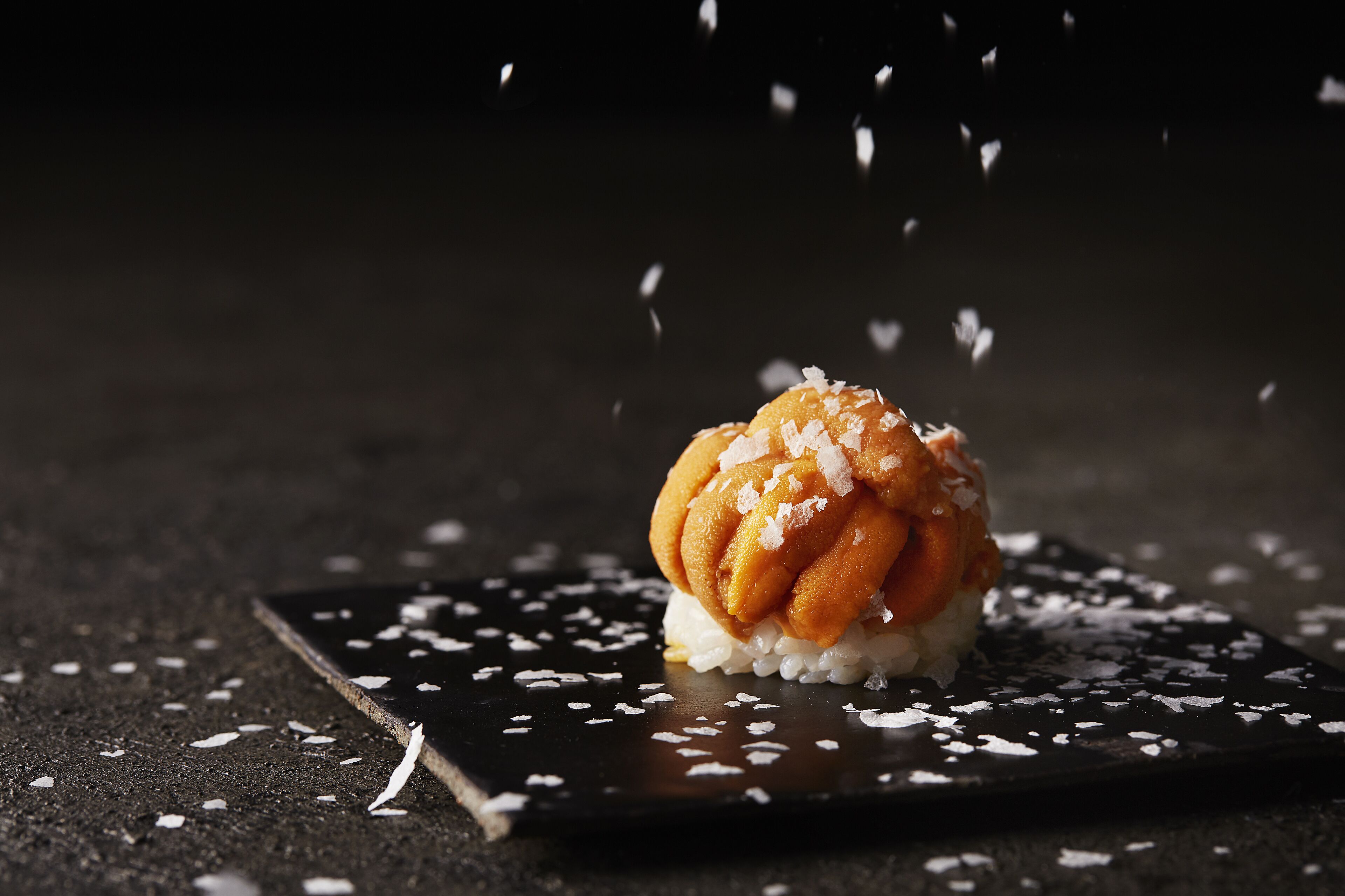 A dessert on a dark plate with scattered sugar crystals.