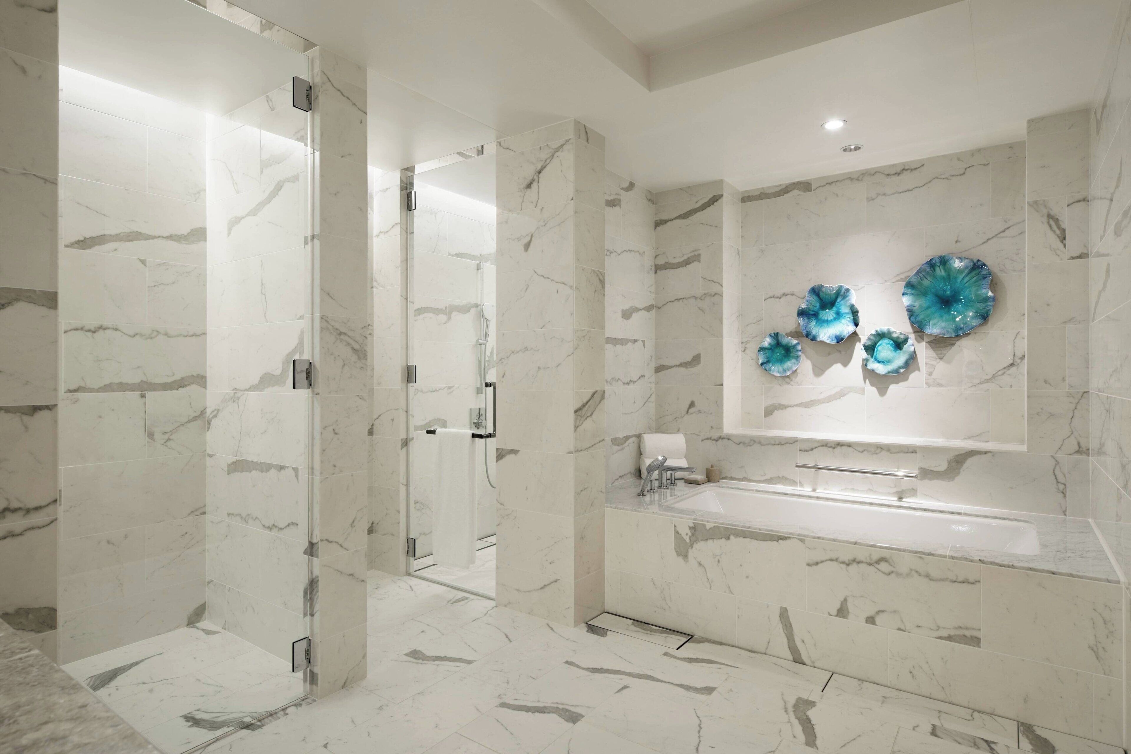 Un baño moderno con ducha de vidrio, piso de baldosas de mármol y un espejo grande con detalles de vidrio decorativos.