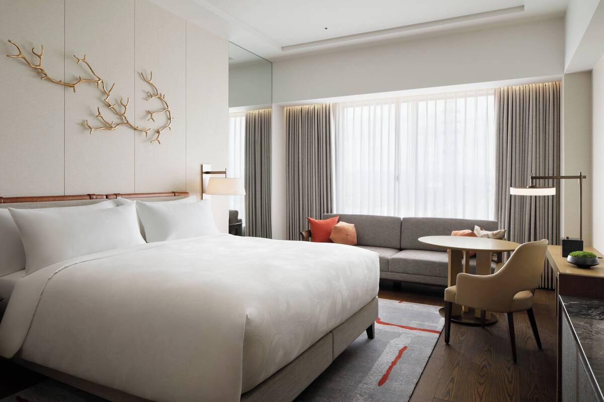 A modern hotel room with a large bed, a sofa, a small table, and a chair.
