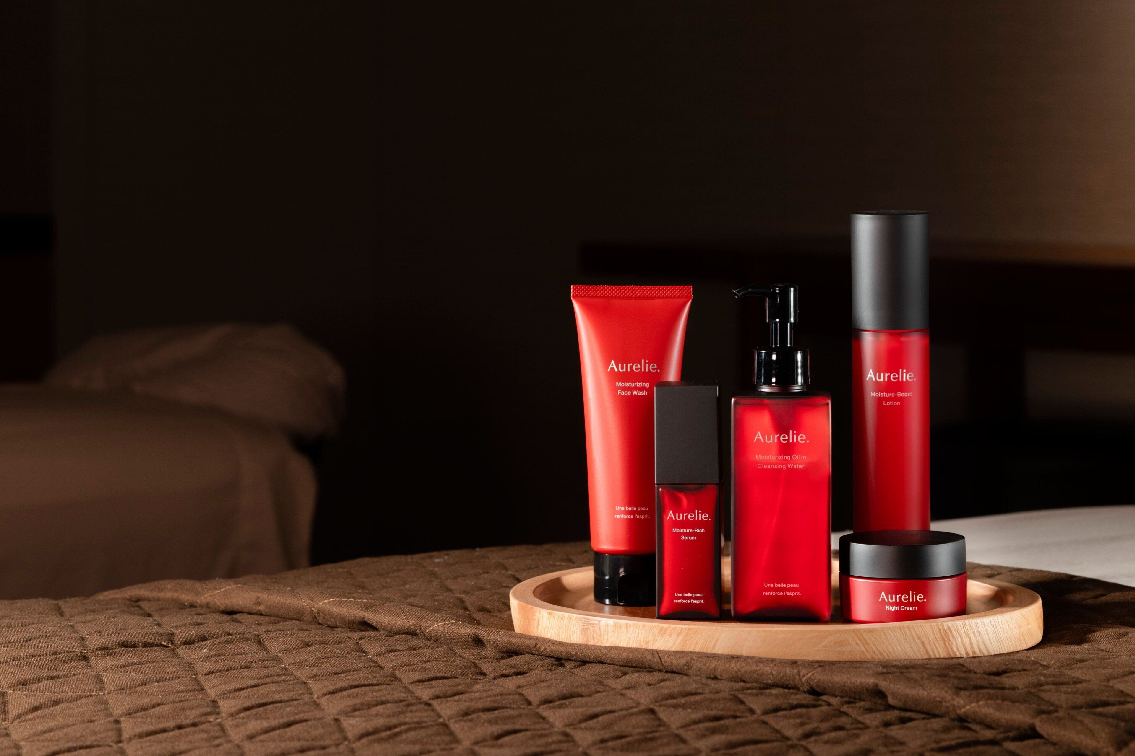 A selection of skincare products arranged on a tray in a dimly lit room with a bed in the background.