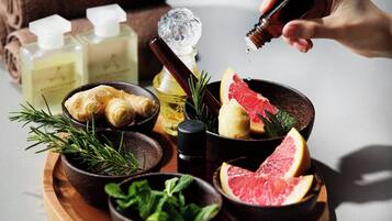 Una bandeja de madera con diversos objetos, entre ellos una botella de líquido, un cuenco de hierbas y rodajas de cítricos.