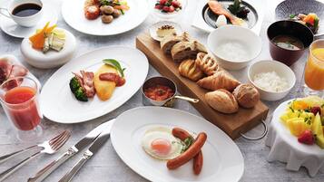A variety of breakfast dishes including eggs, sausages, croissants, and fruit on a table.