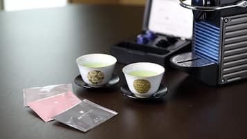 Two cups with a decorative design, a coffee machine, and packets on a table.