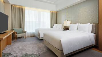 A hotel room with two beds, a desk, a chair, a TV, and a large window with curtains.