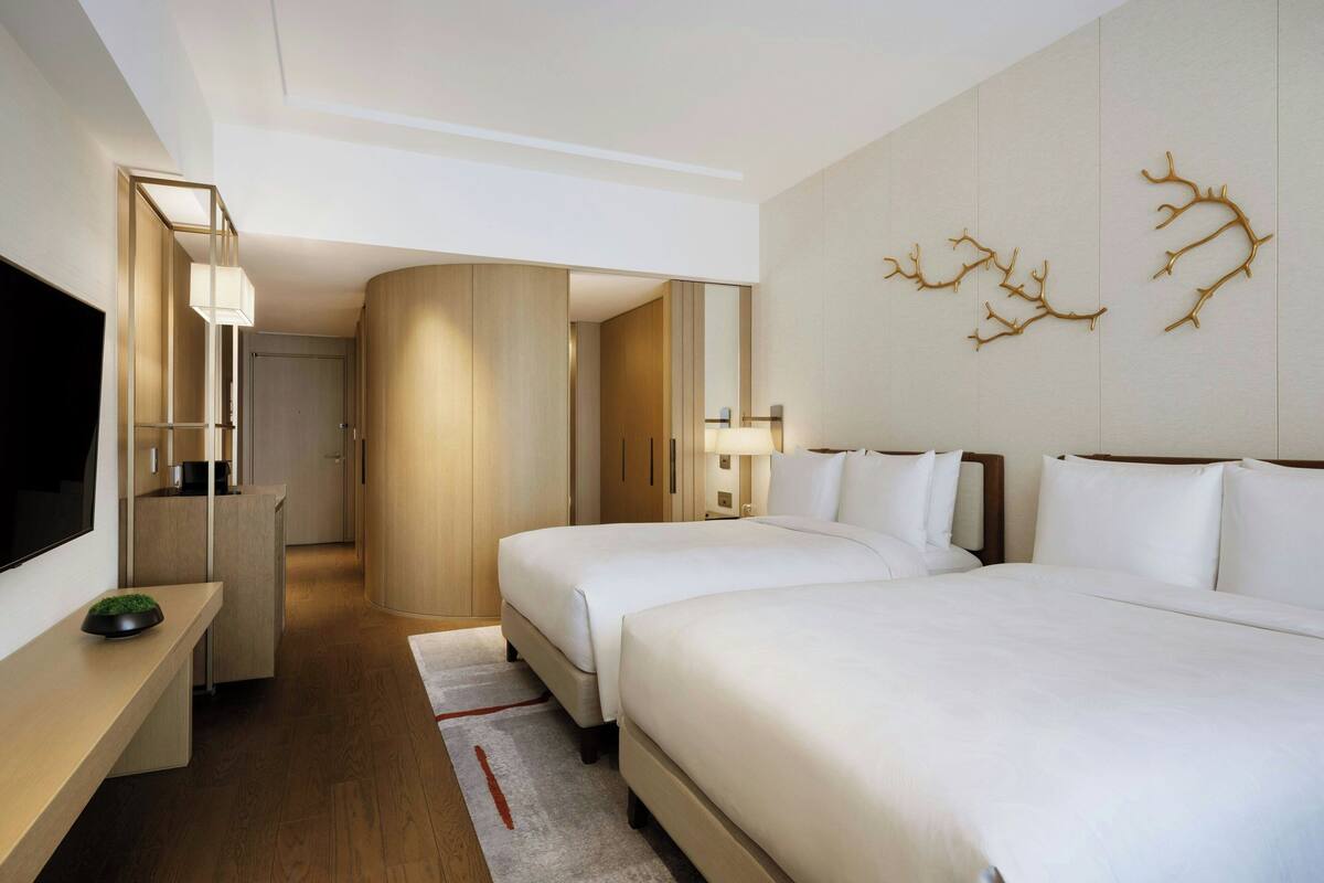 A hotel room with two beds, a TV, a desk, and a mirror.
