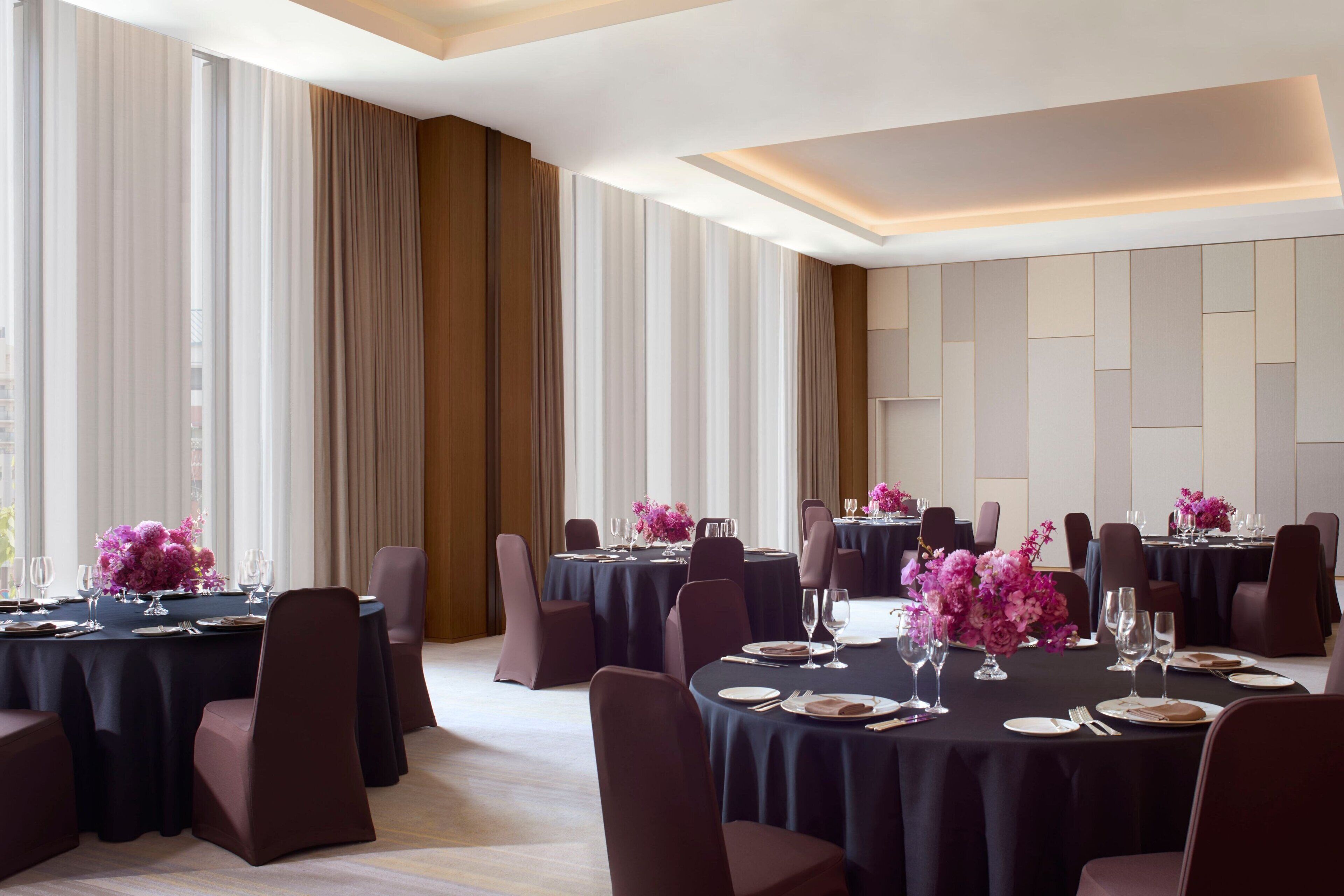 A formal dining room with round tables, dark tablecloths, and purple floral centerpieces.