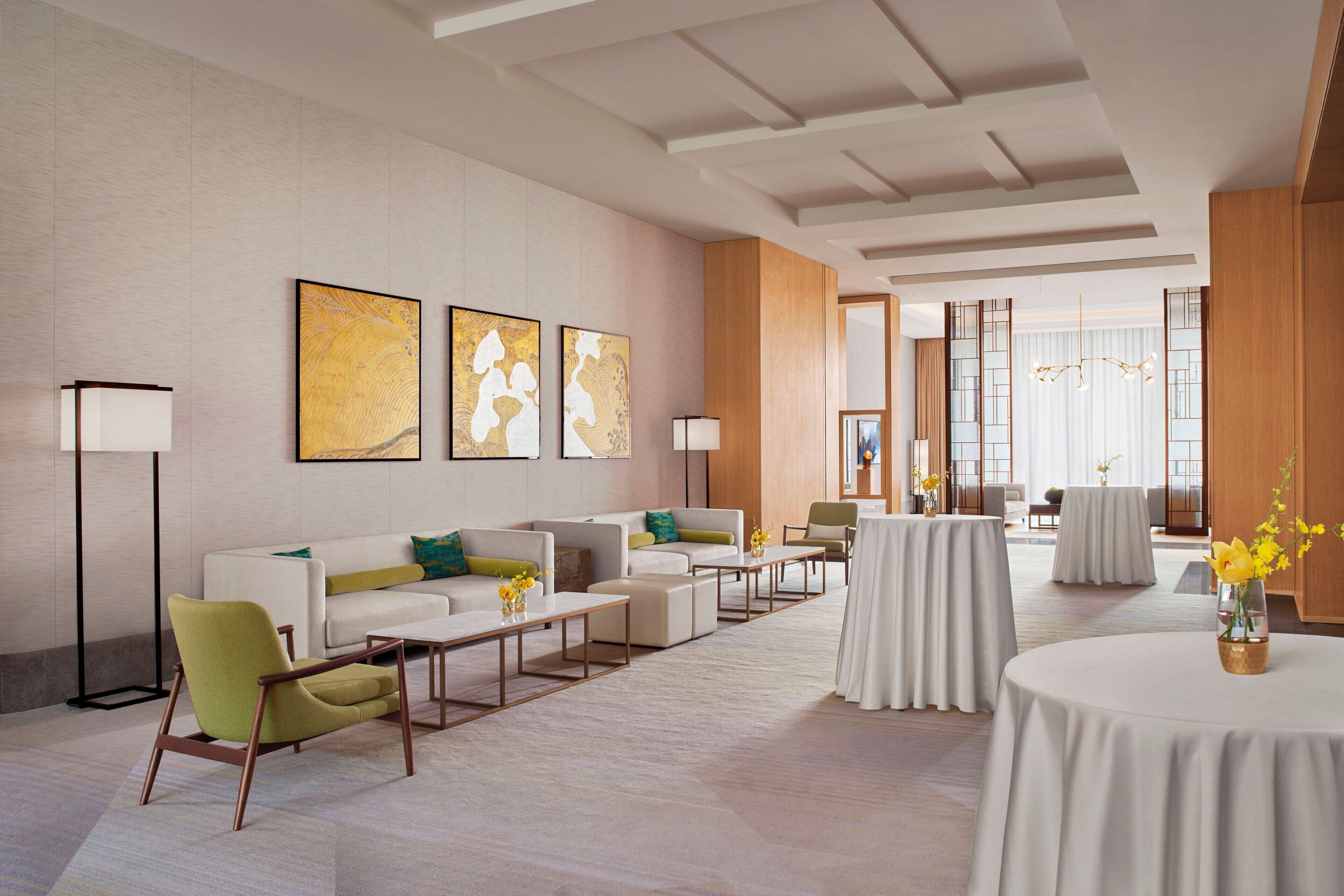 Eine großzügige Lobby mit modernem Design, ausgestattet mit einer Couch, Sesseln, einem Couchtisch und einem runden Tisch mit Blumenvase.