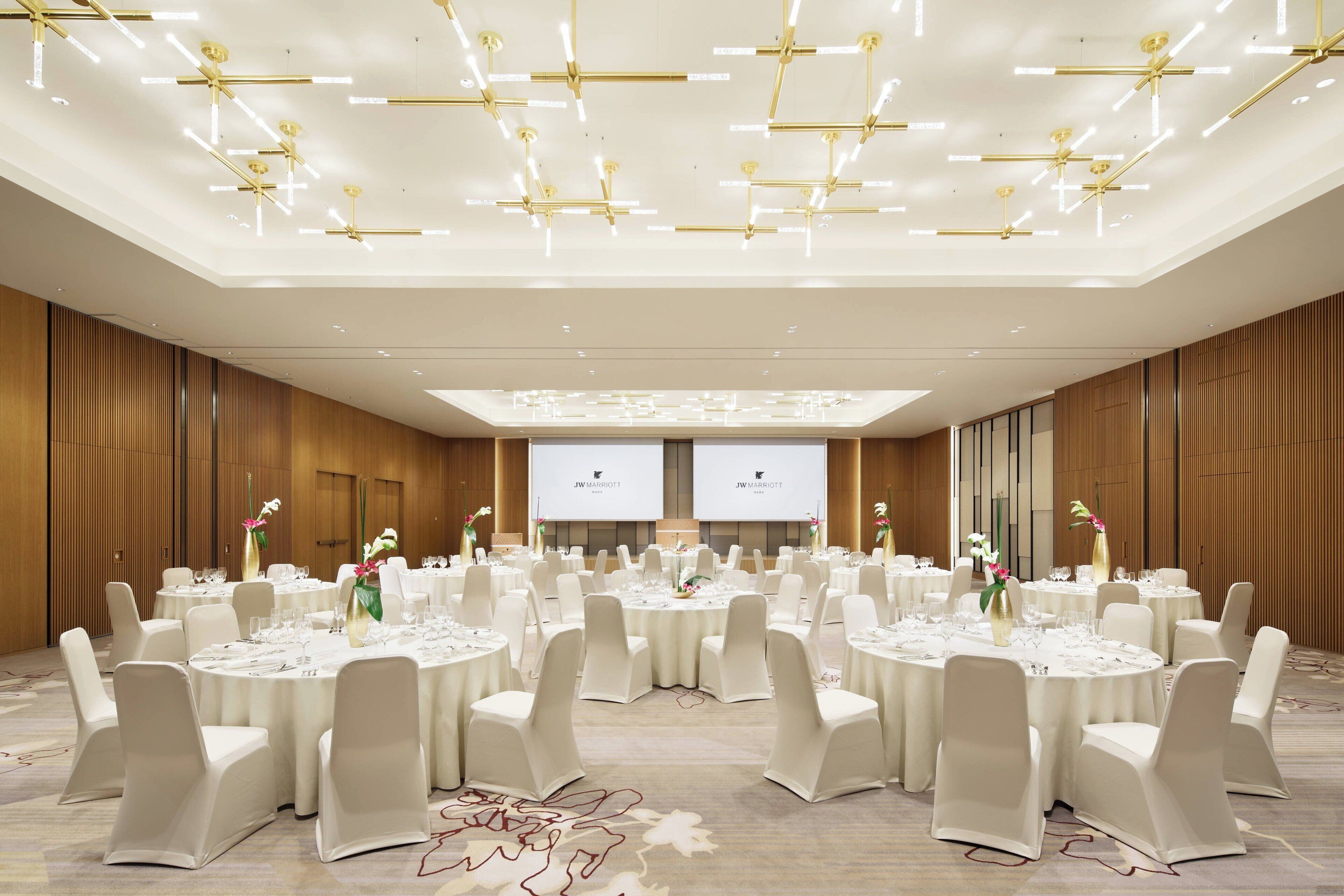 A large conference room with round tables, white chairs, and a modern chandelier.