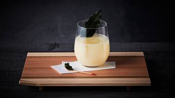 A glass of a light-colored beverage on a wooden tray with a dark background.