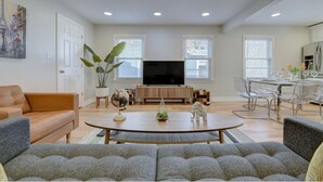 Een moderne woonkamer met een bank, een salontafel, een televisie en een eethoek met transparante stoelen.