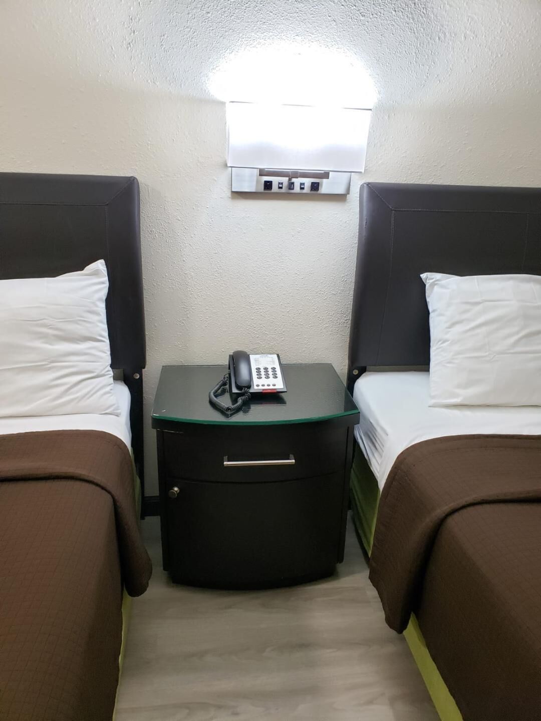 Ein Hotelzimmer mit zwei Betten, einem Nachttisch mit Telefon und einer Wand-Klimaanlage.