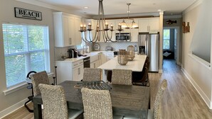 A modern kitchen with white cabinets, a central island, and wicker chairs.